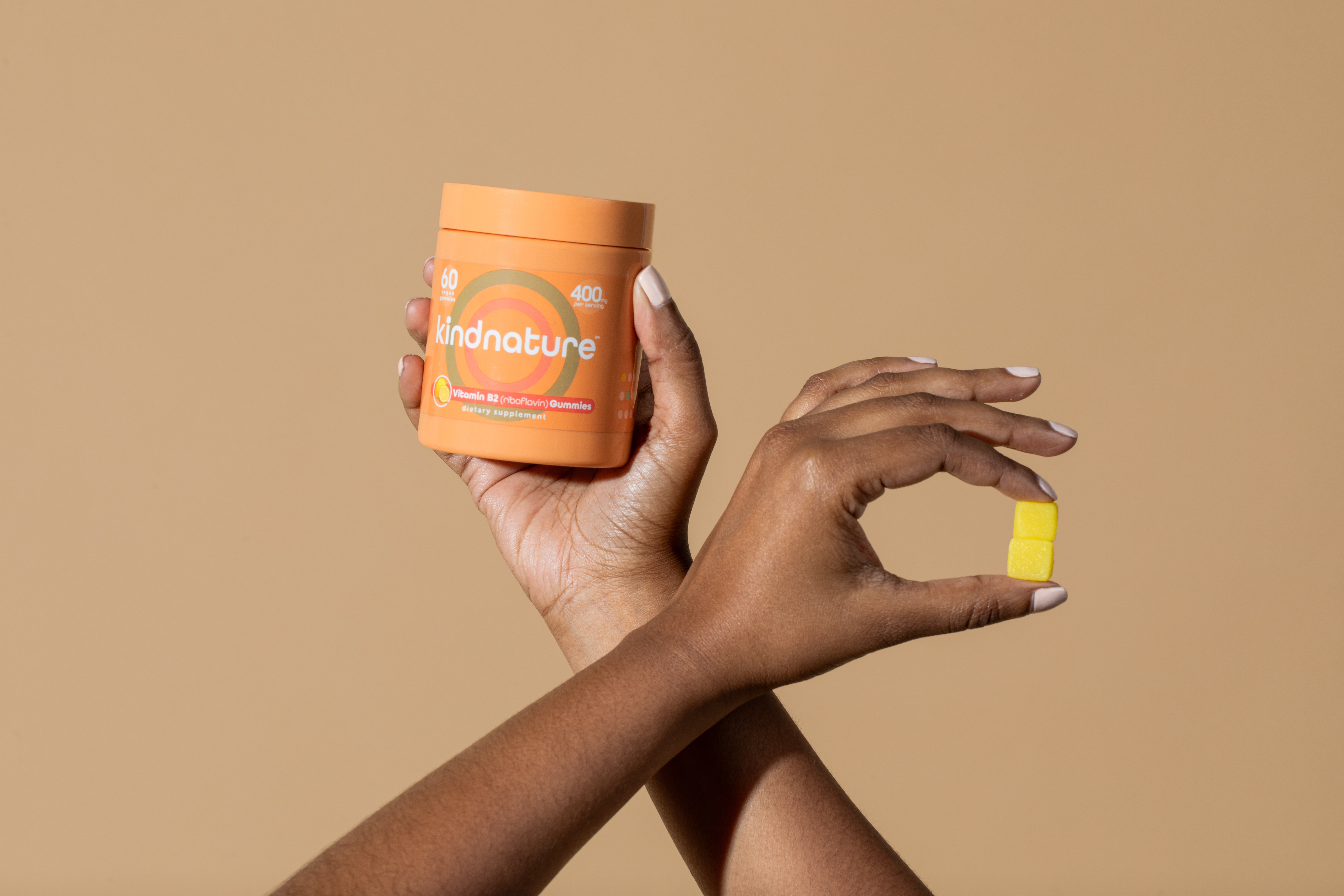 Hands holding KINDNATURE B2 Riboflavin bottle with a single yellow gummy