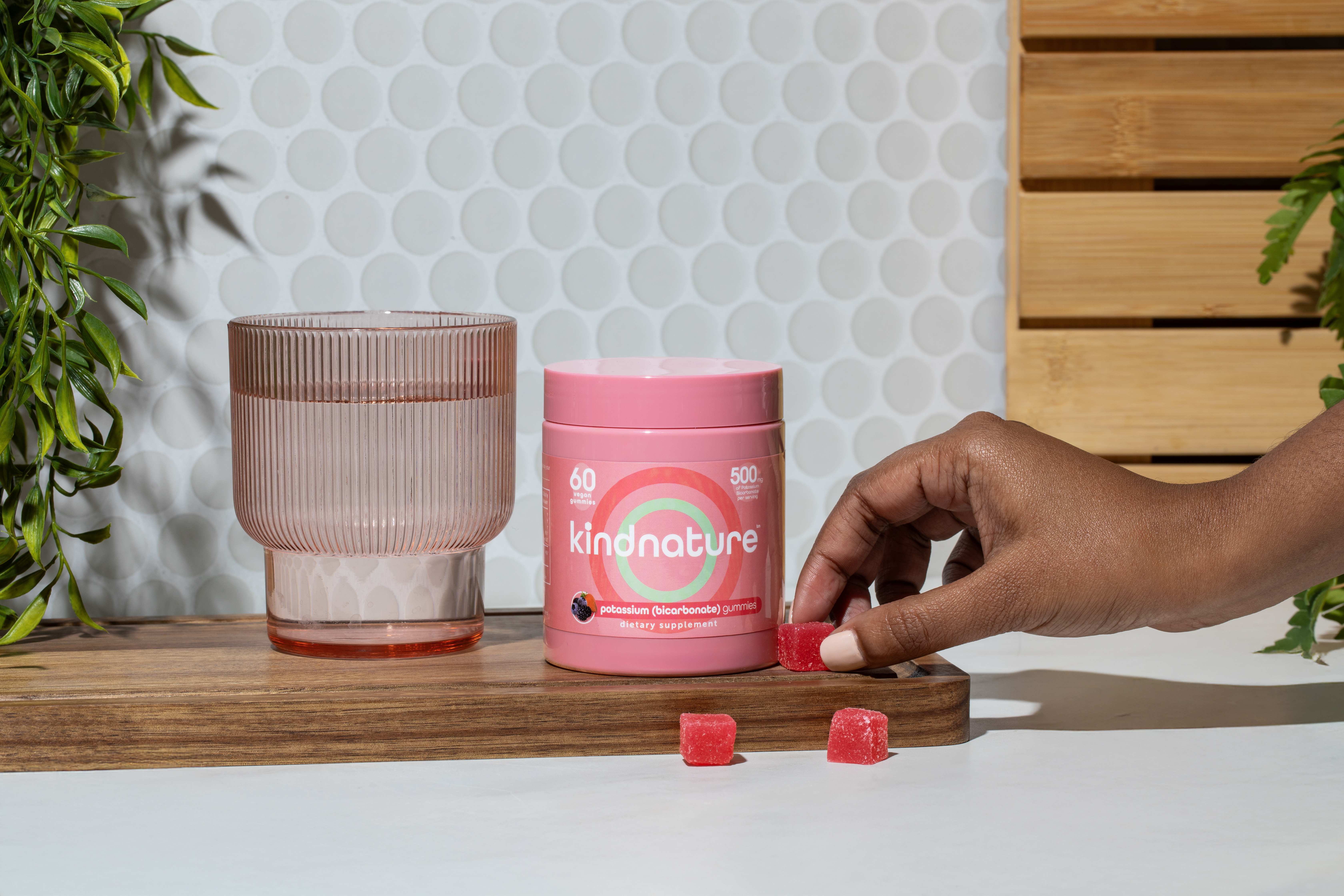 KINDNATURE Potassium Bicarbonate gummies on wooden surface with hand reaching for gummies