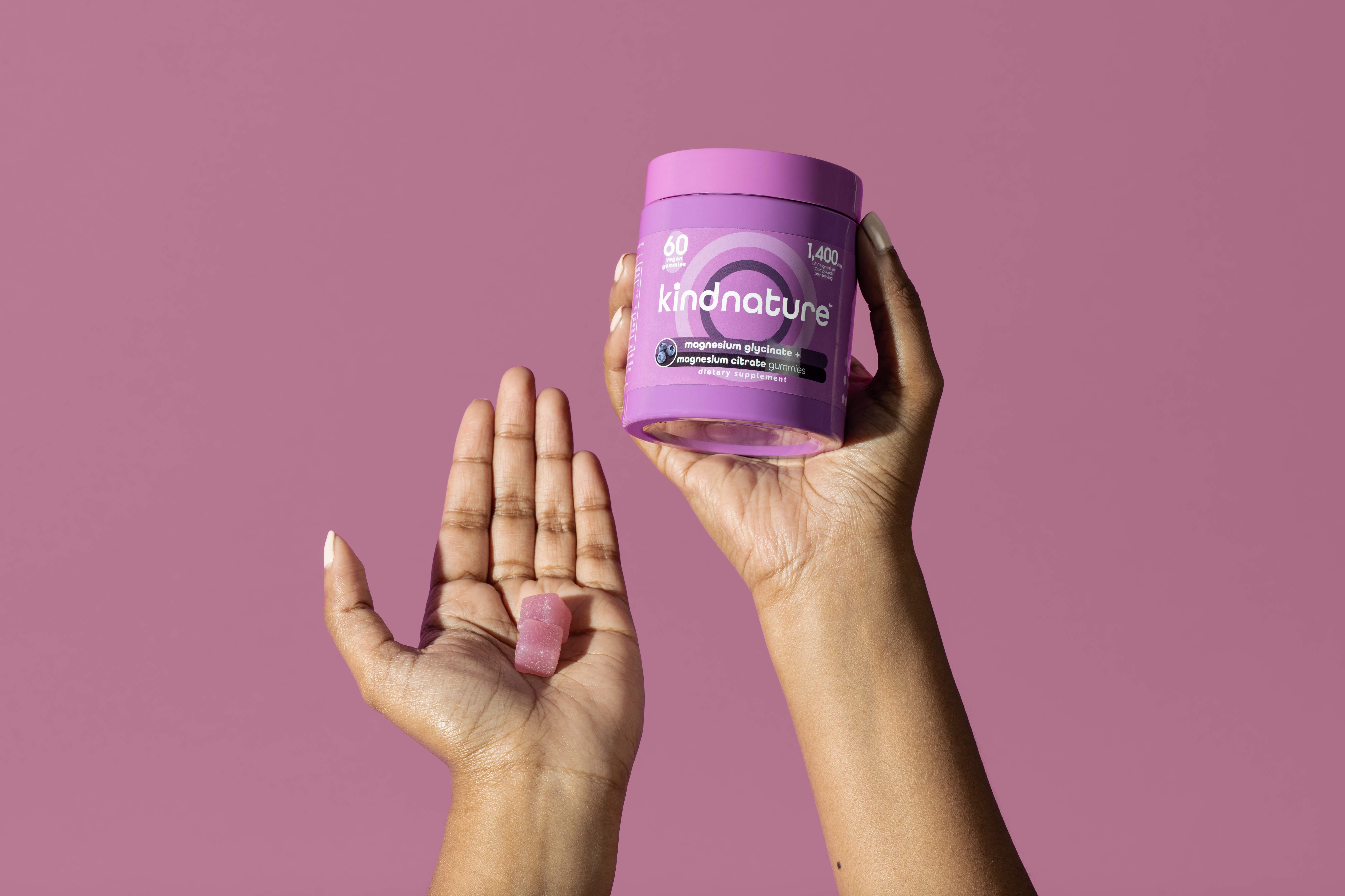 Hand holding KINDNATURE Magnesium gummies bottle with pink gummy on palm