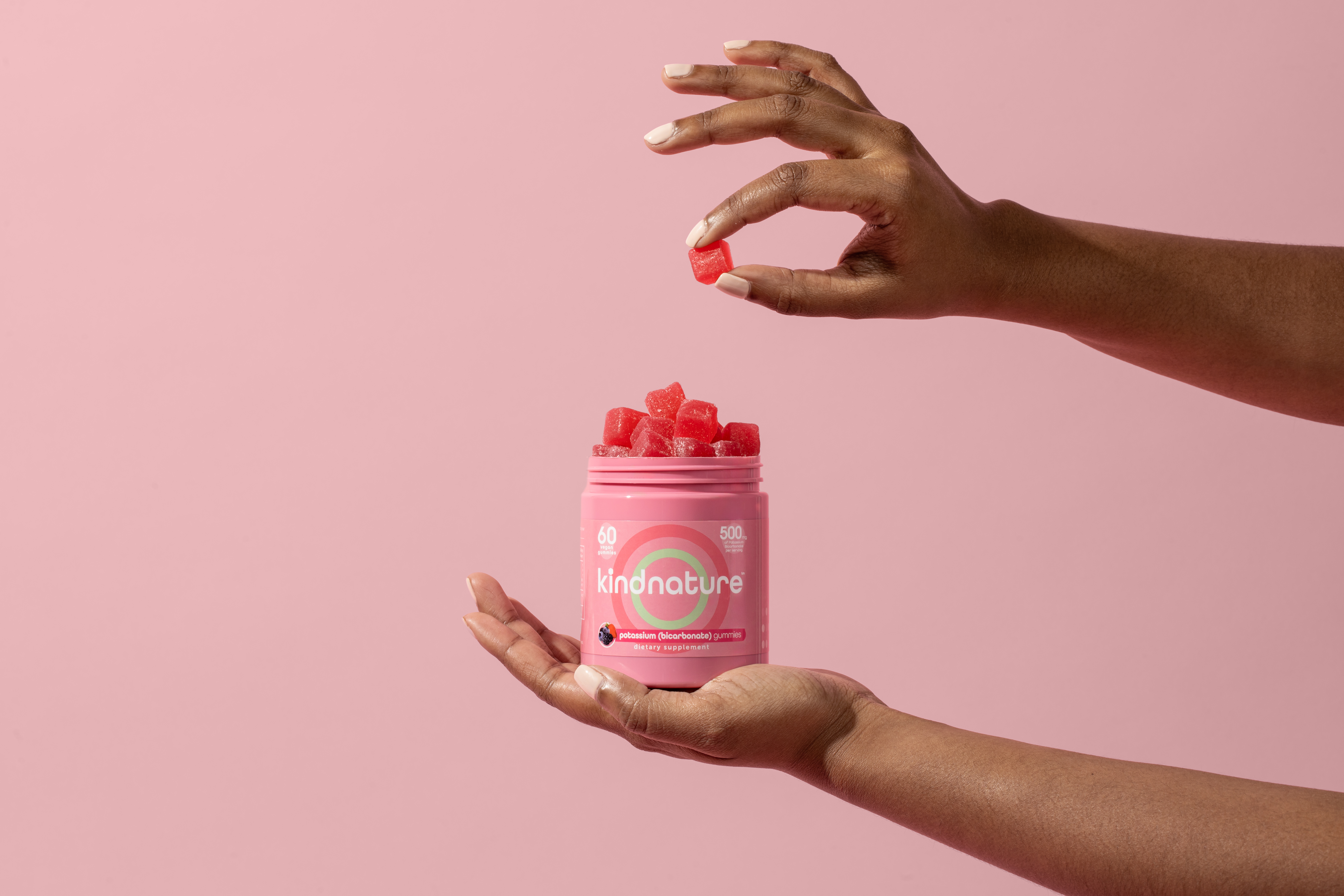 Hands holding KINDNATURE Potassium Bicarbonate bottle with red gummies